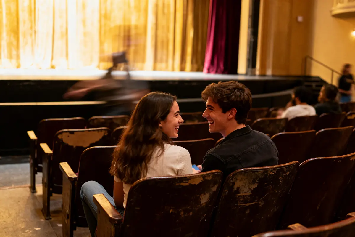 Un couple souriant assis dans une salle de théâtre face à la scène vide illuminée.