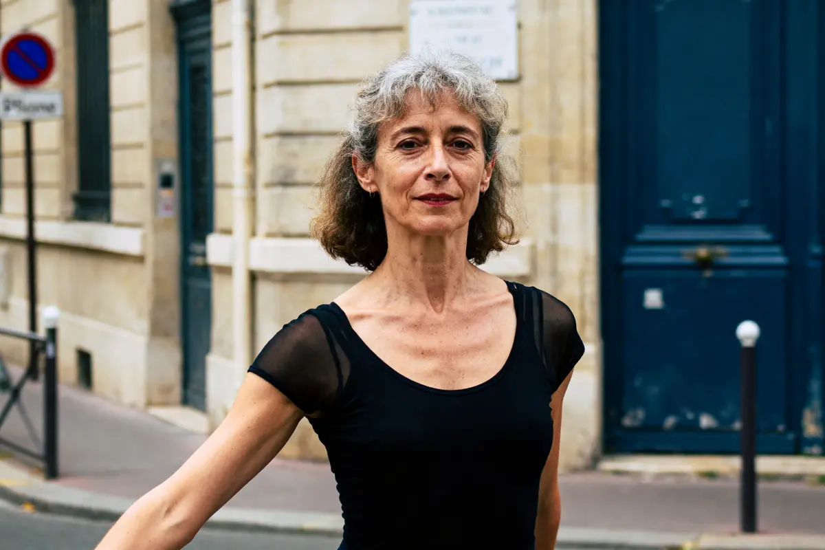 Femme posant devant un bâtiment urbain, portant un top noir.