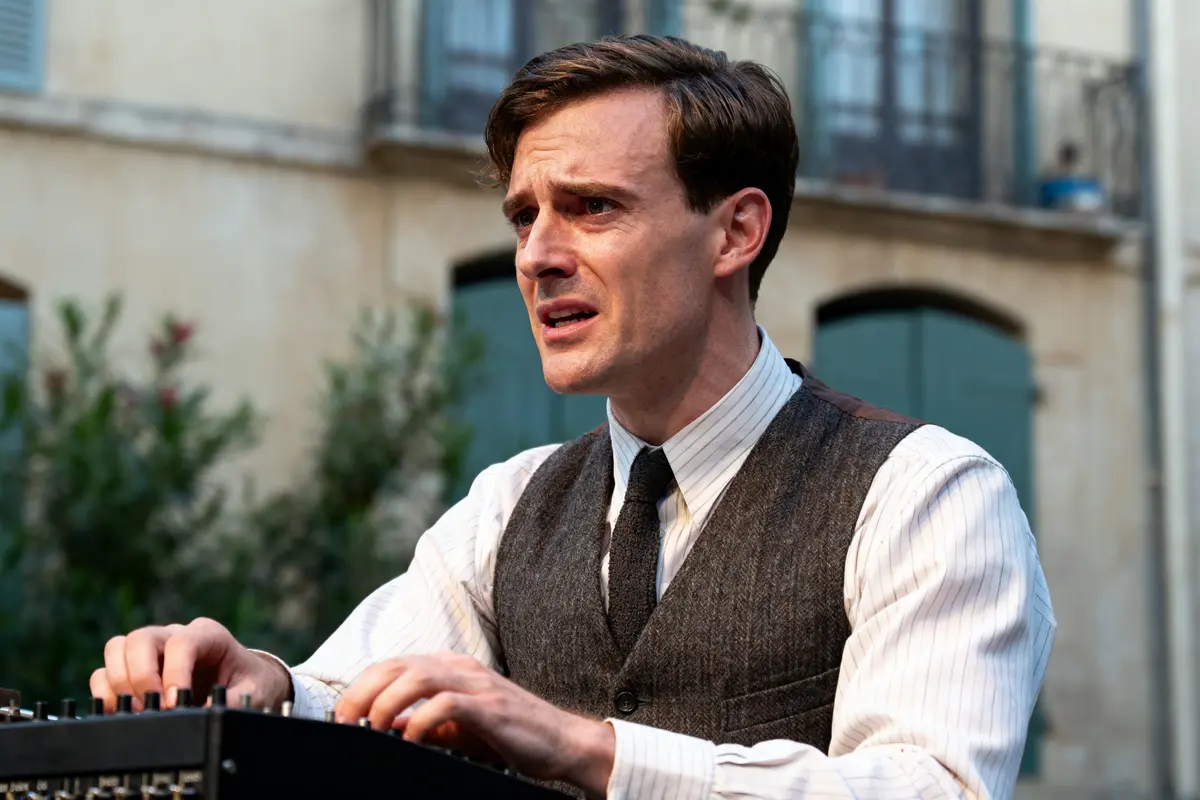 Homme en costume vintage tapant sur une machine, arrière-plan urbain flou, expression concentrée.