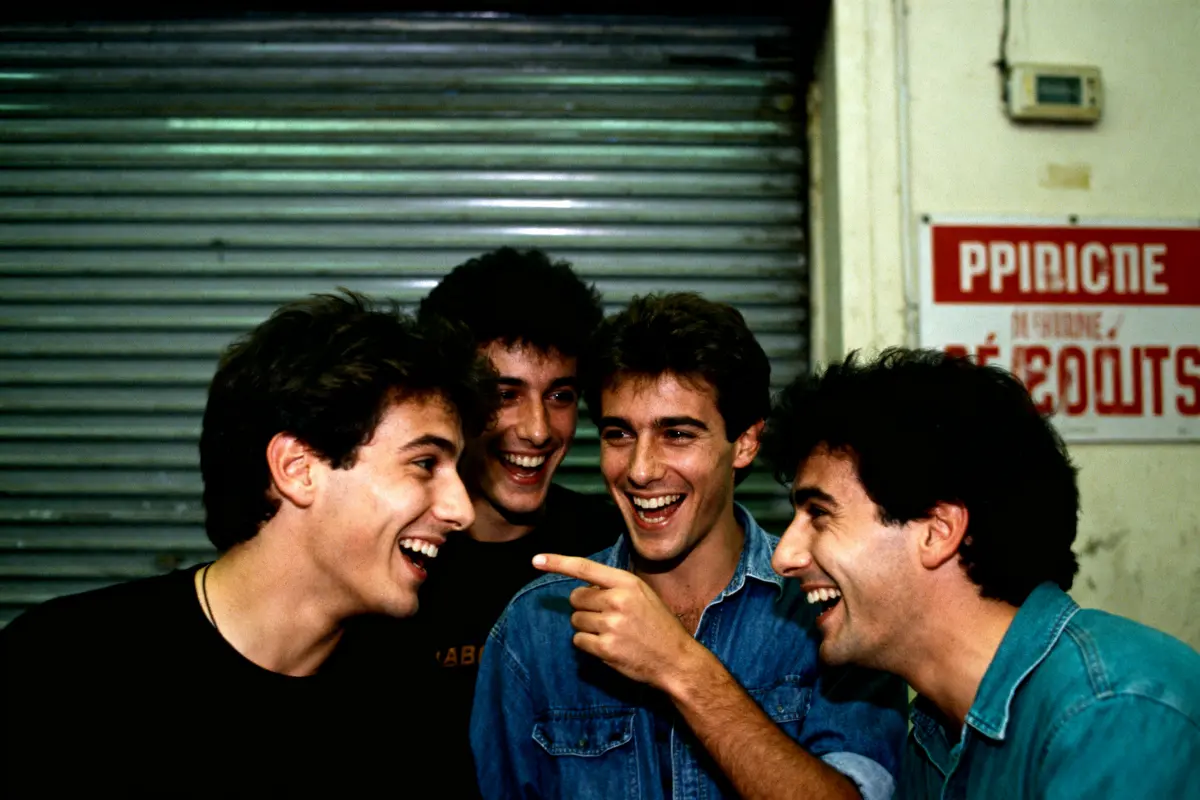 Quatre hommes souriants discutent et rient devant un rideau métallique, ambiance détendue et conviviale.