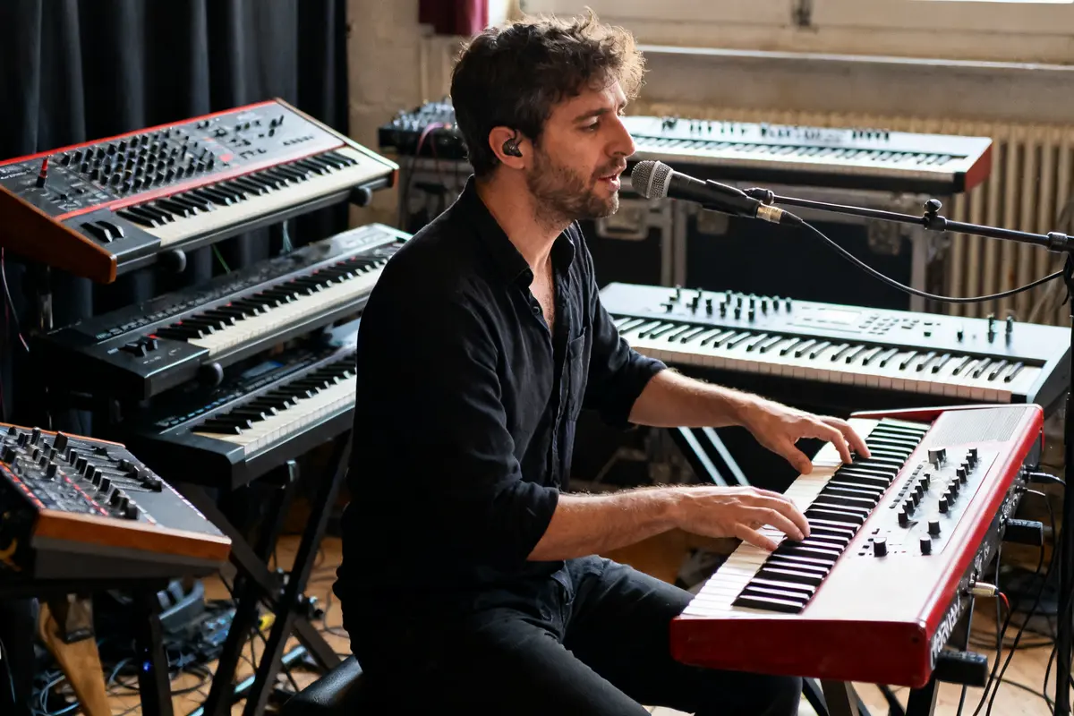 Homme jouant du clavier en studio entouré de synthétiseurs Renaud Bizart-Vincent accompagne au microphone
